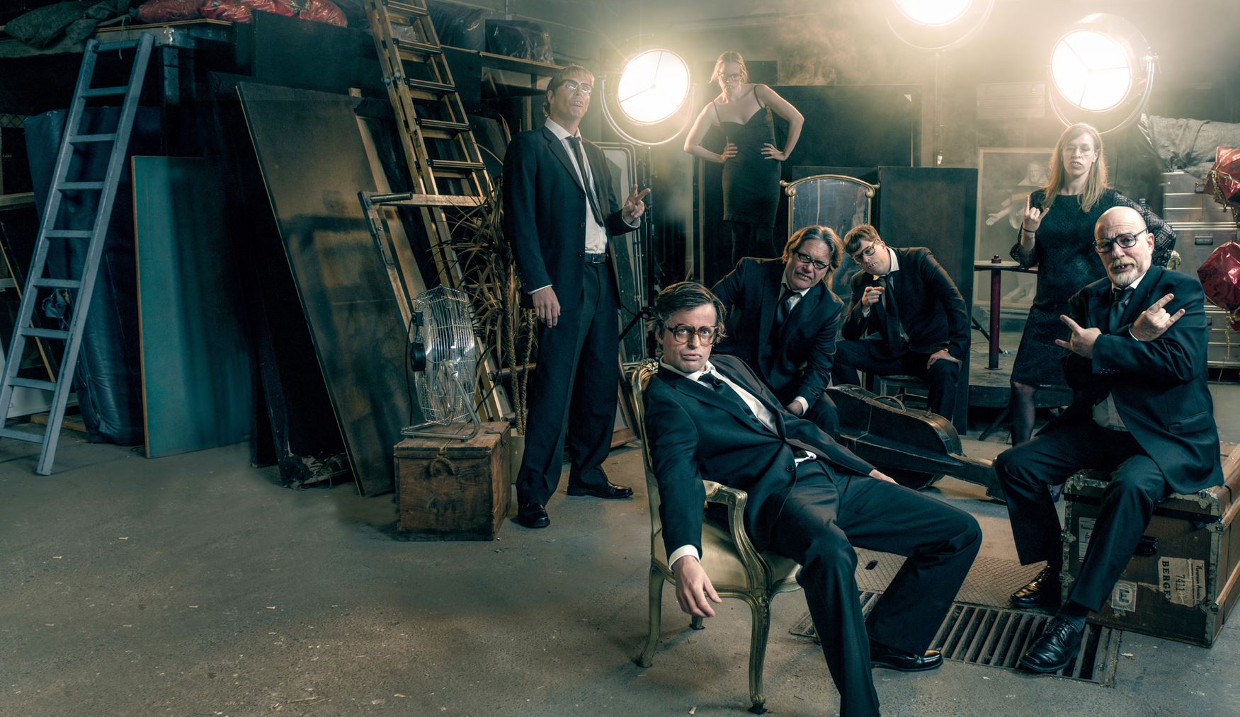 Plakatfoto Nerdene. Skuespillere kledd i mørk dress og kjole og med løstenner.