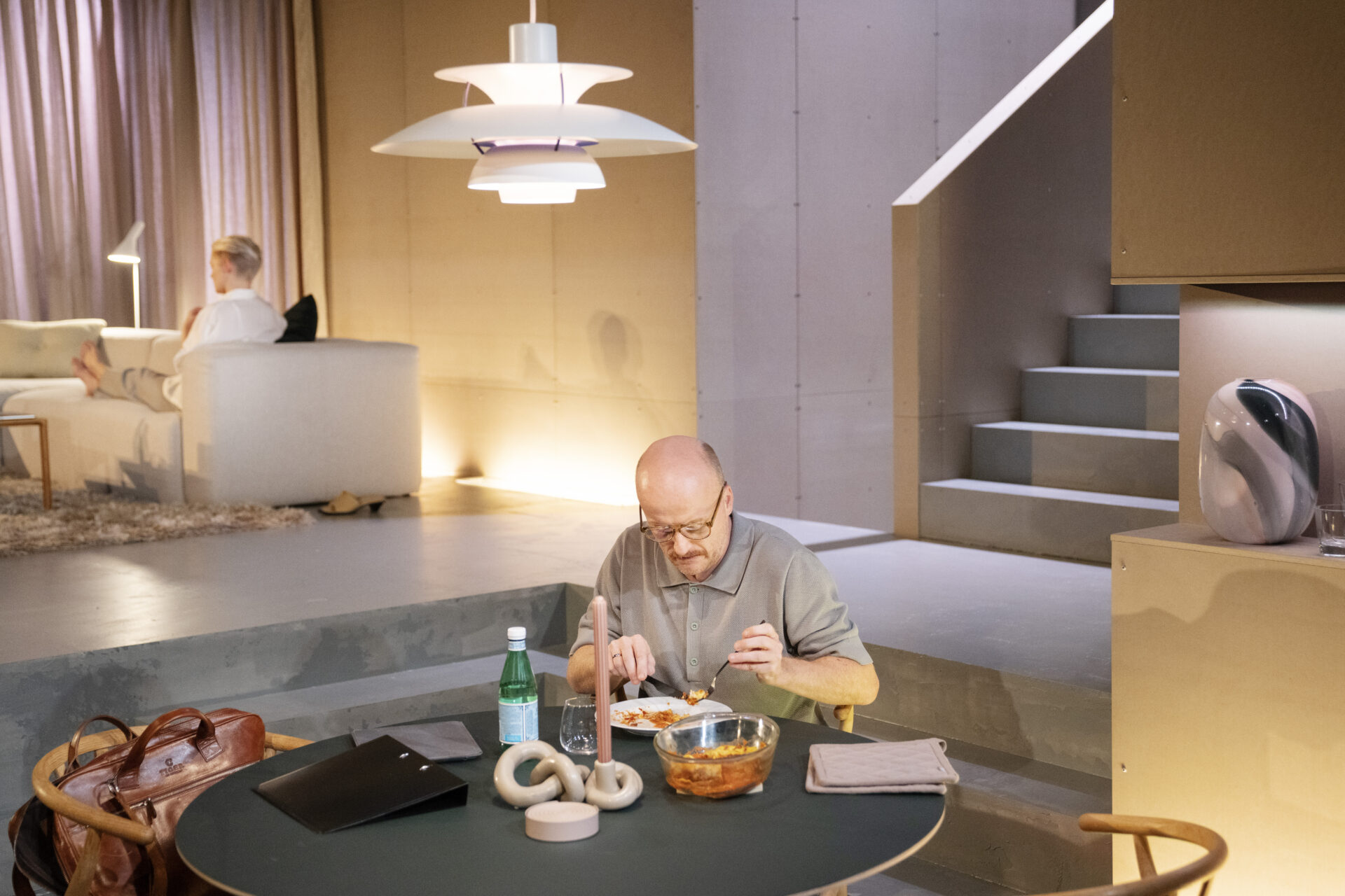 Daniel sitter og spiser lasagne for seg selv ved kjøkkenbordet mens Sibylle sitter alene borte i sofaen