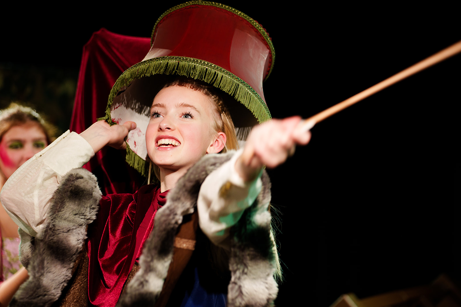 Jente som holder en lampeskjerm over hodet med den ene hånden, og holder en tryllestav i den andre hånden med utstrakt arm