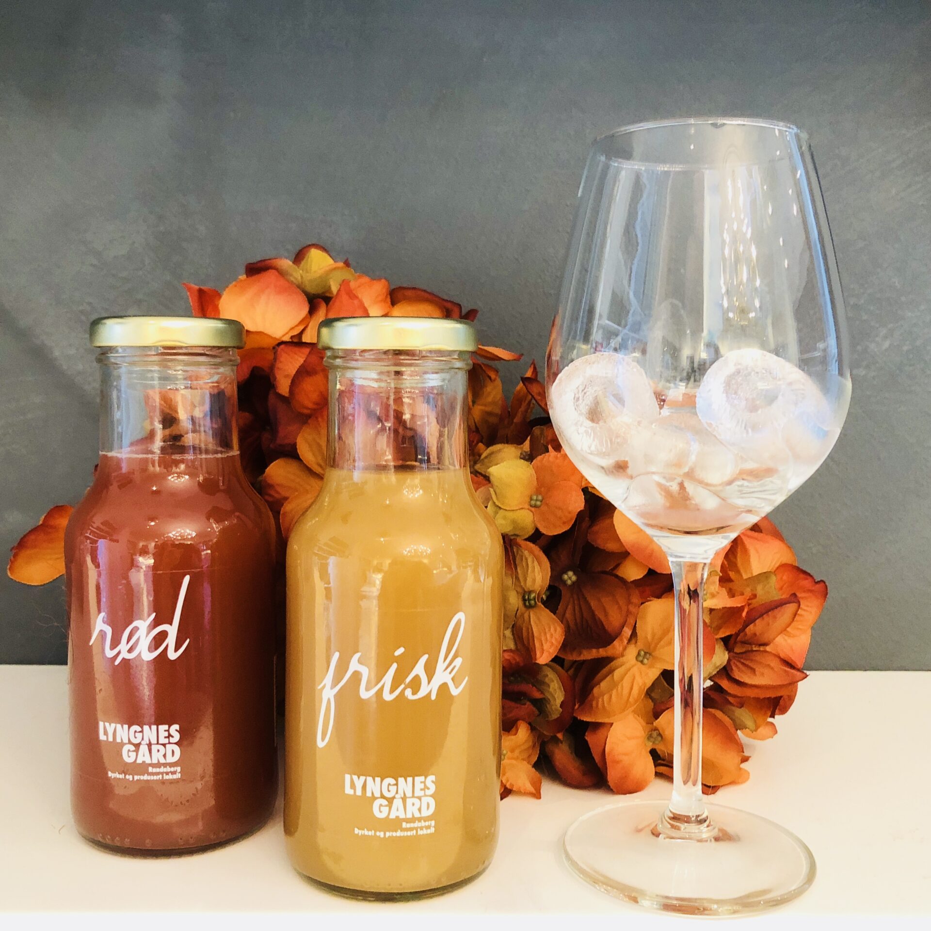 Glass med isbiter og to flasker med eplemost ved siden av.