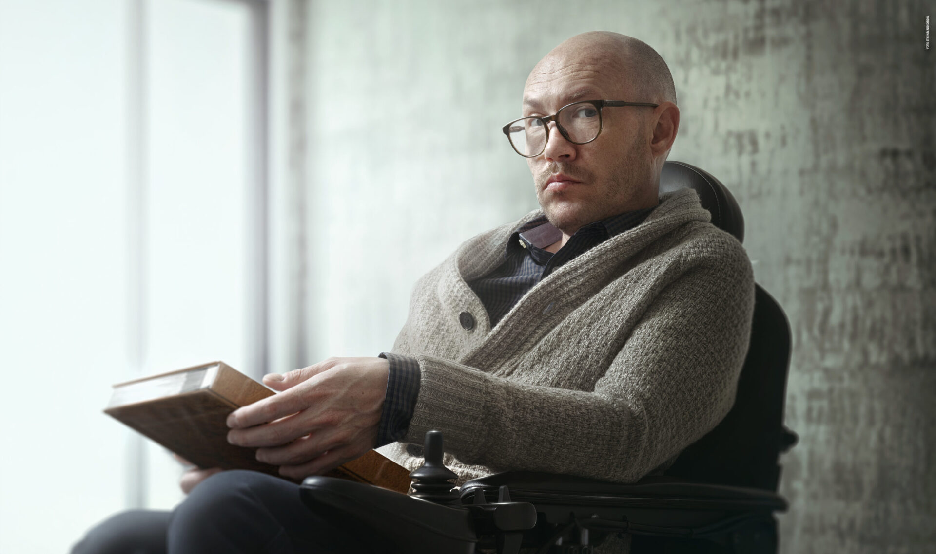 En mann sitter med en bok i en rullestol