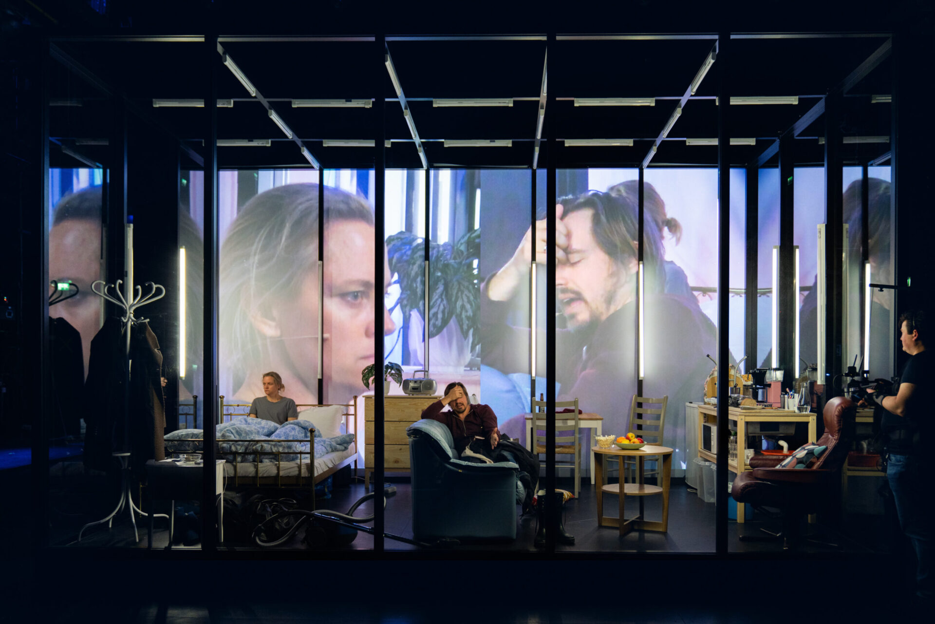 En kvinne i en seng og en mann i en lenestol filmes og vises på en storskjerm