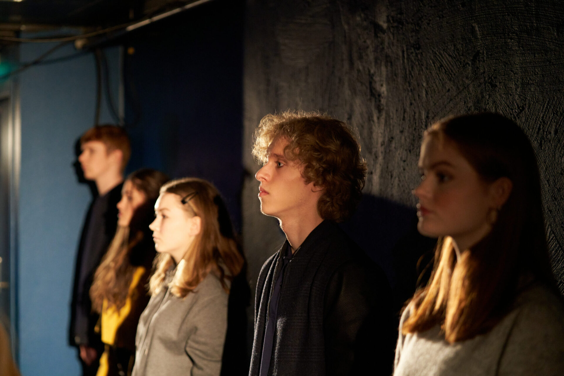 Fem ungdommer står inntil en vegg