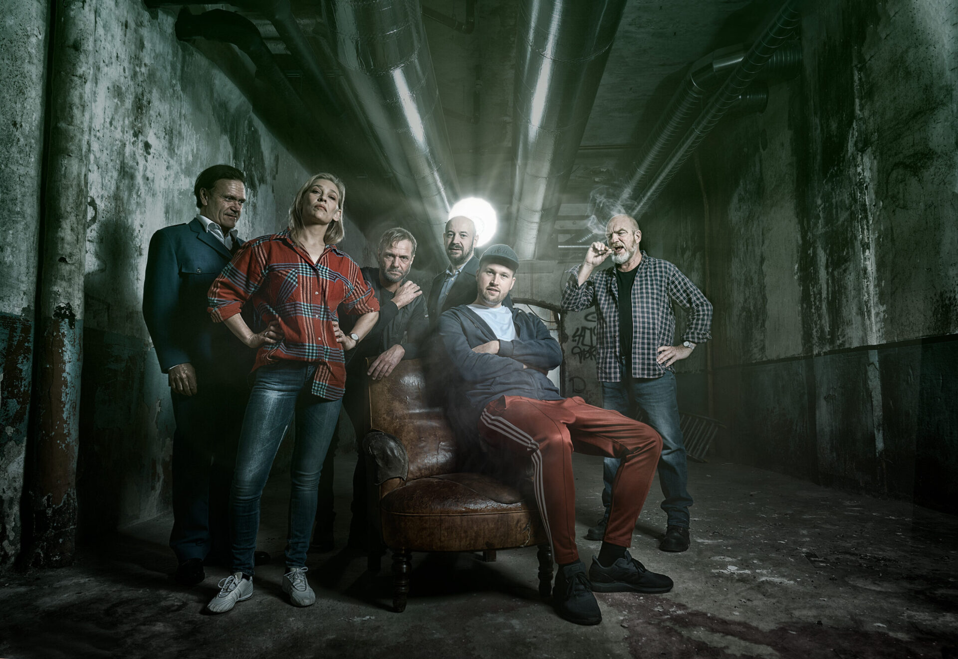 Fem menn, en sliten lenestol og en kvinne i et fabrikklokale.