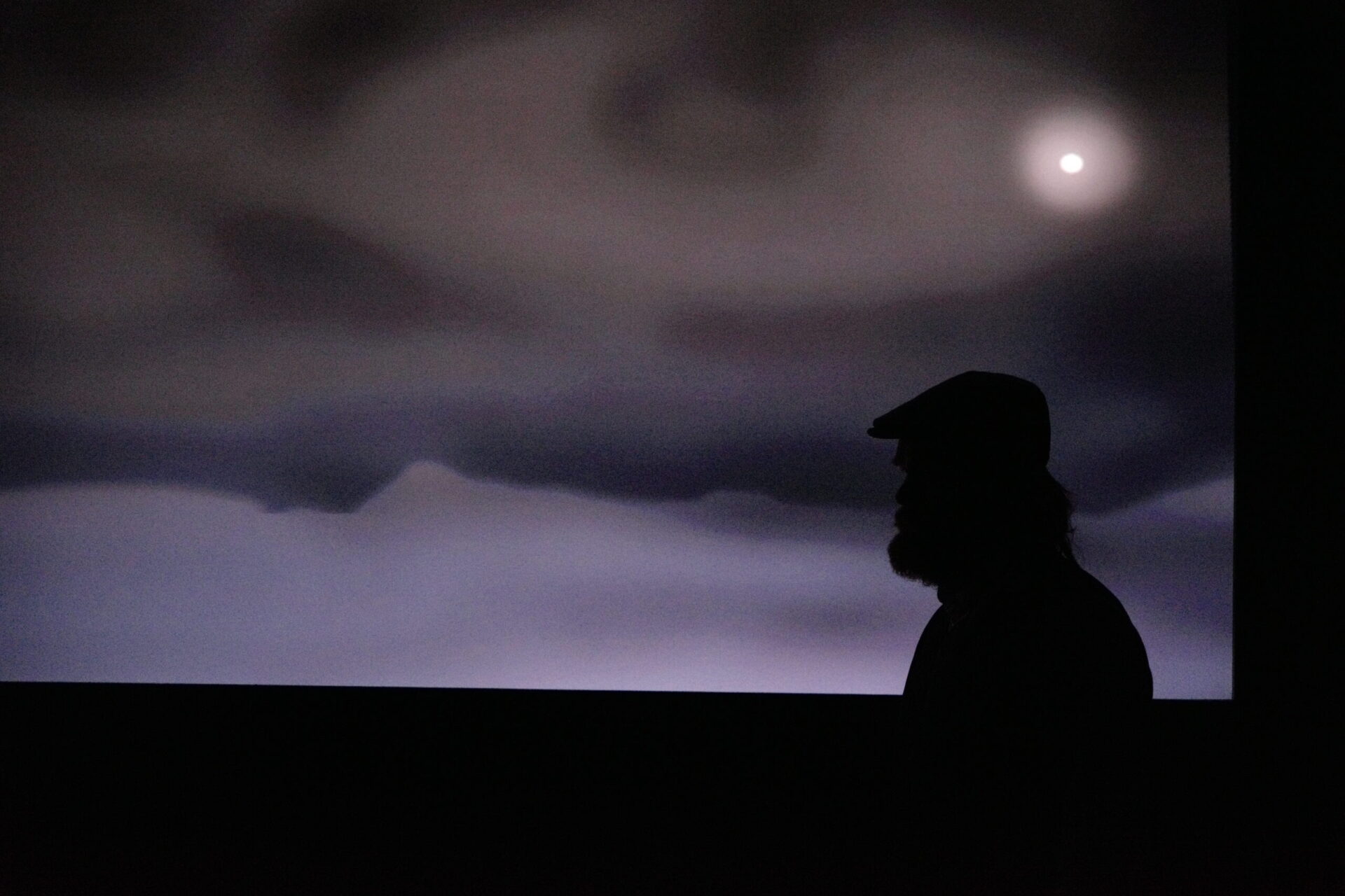 Siluetten av en mann med caps mot en mørk himmel med måne.