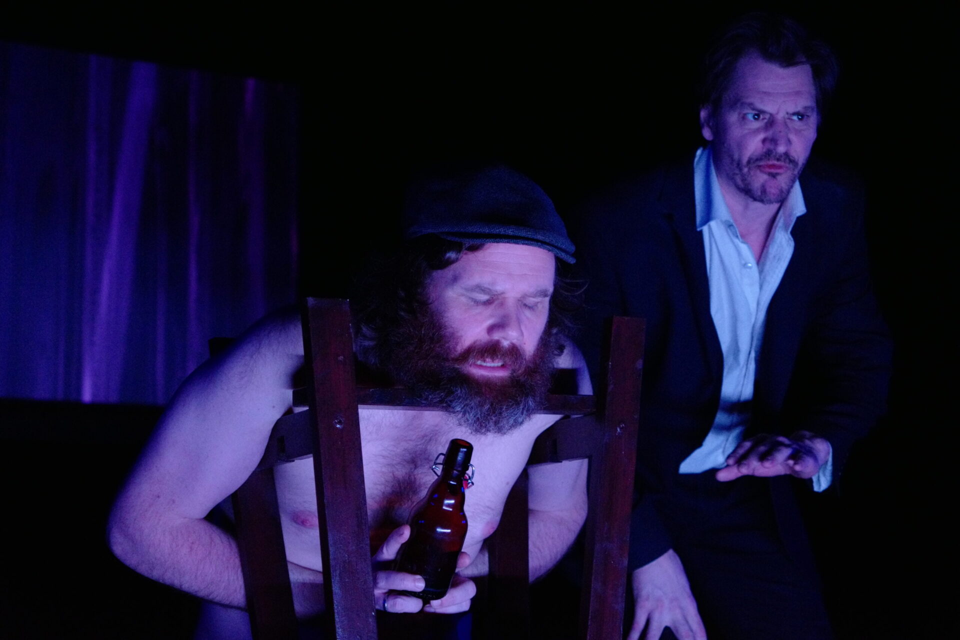 En mann har det vondt og er fanget i en stol. En annen mann står ved siden av.