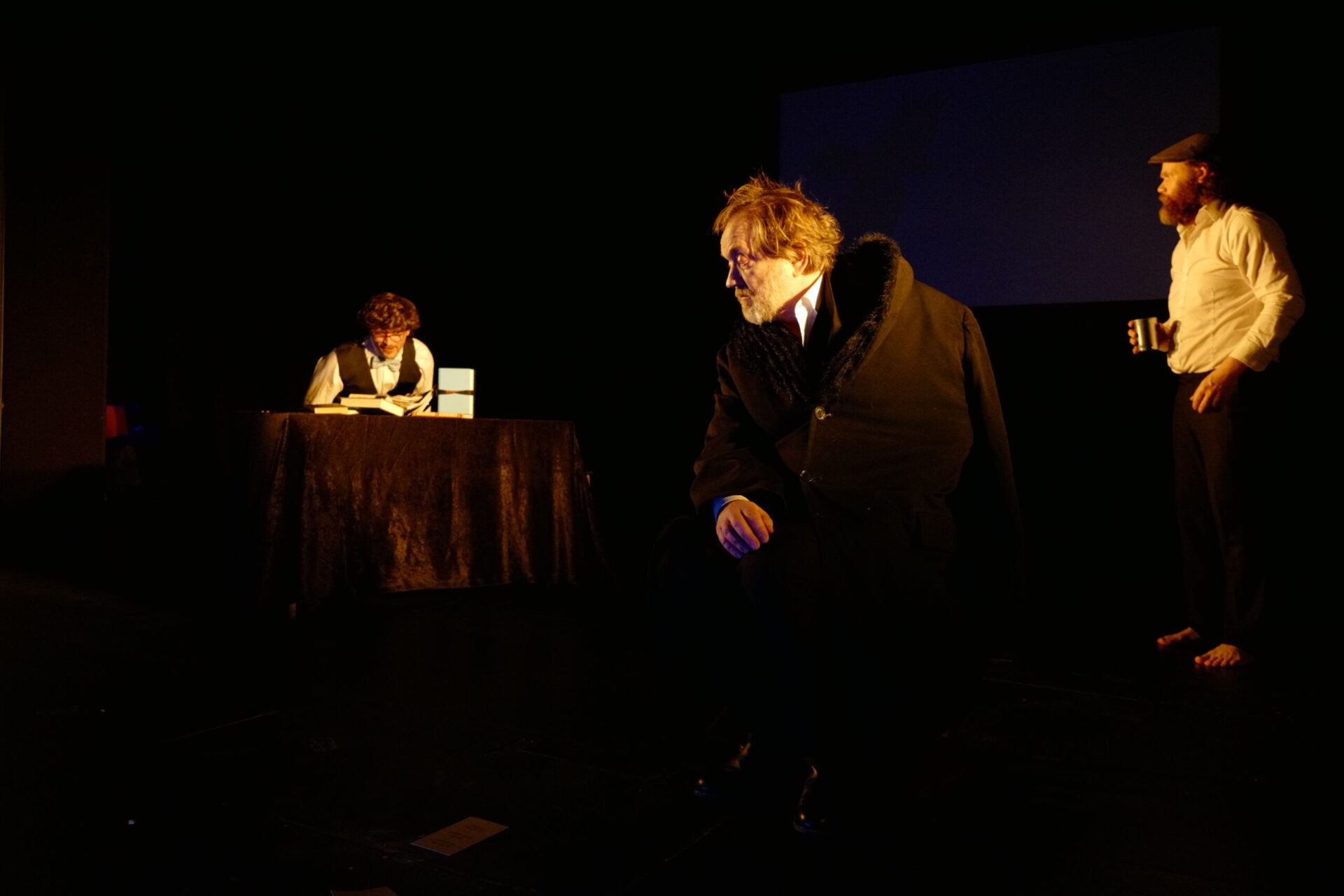 Tre menn i et rom. Den ene sitter og leser.