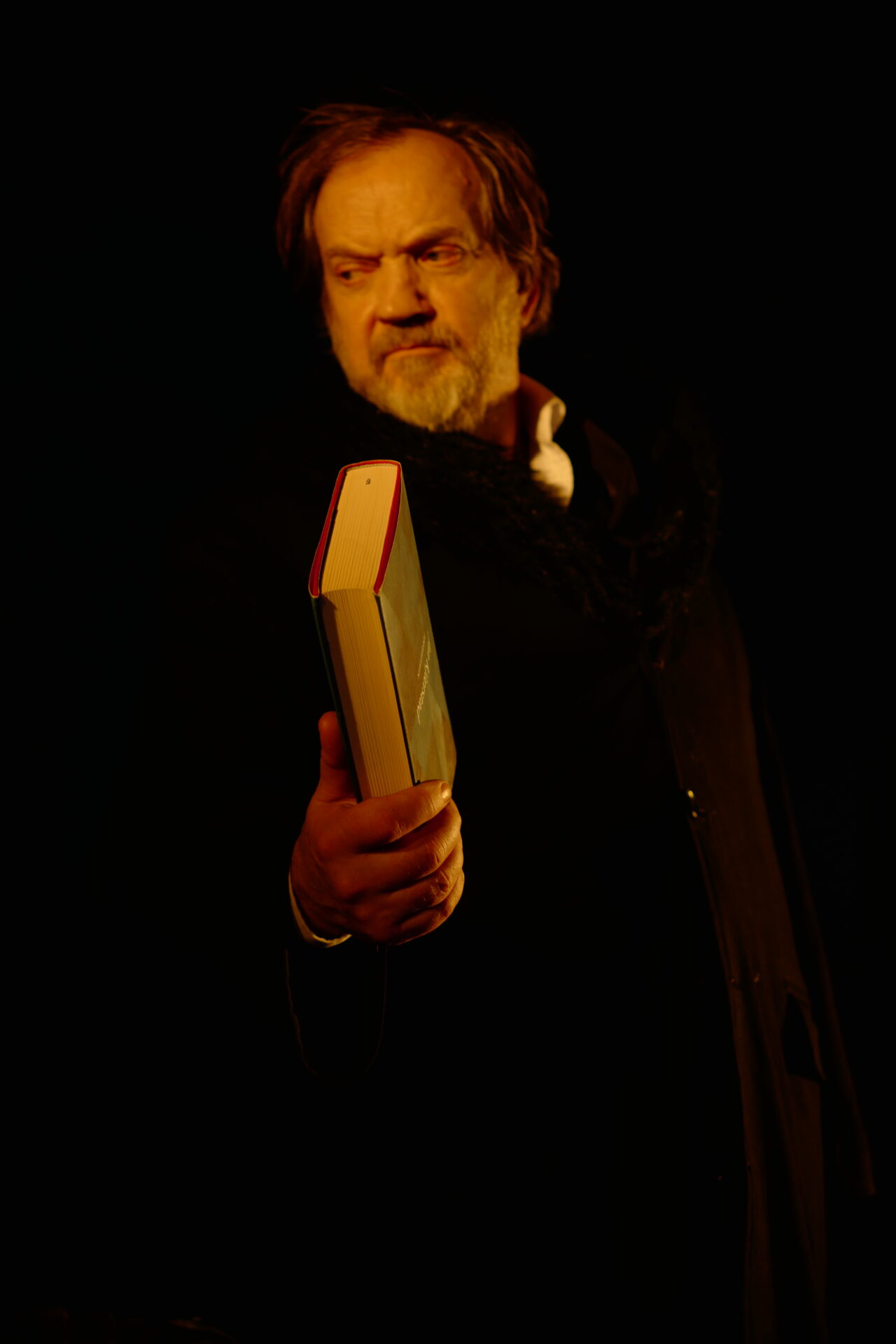 En sint mann i mørke klær med en bok i hånden.