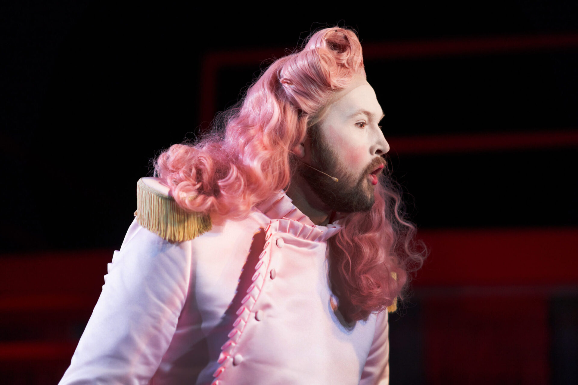En hoffmann i rosa klær og rosa parykk synger.