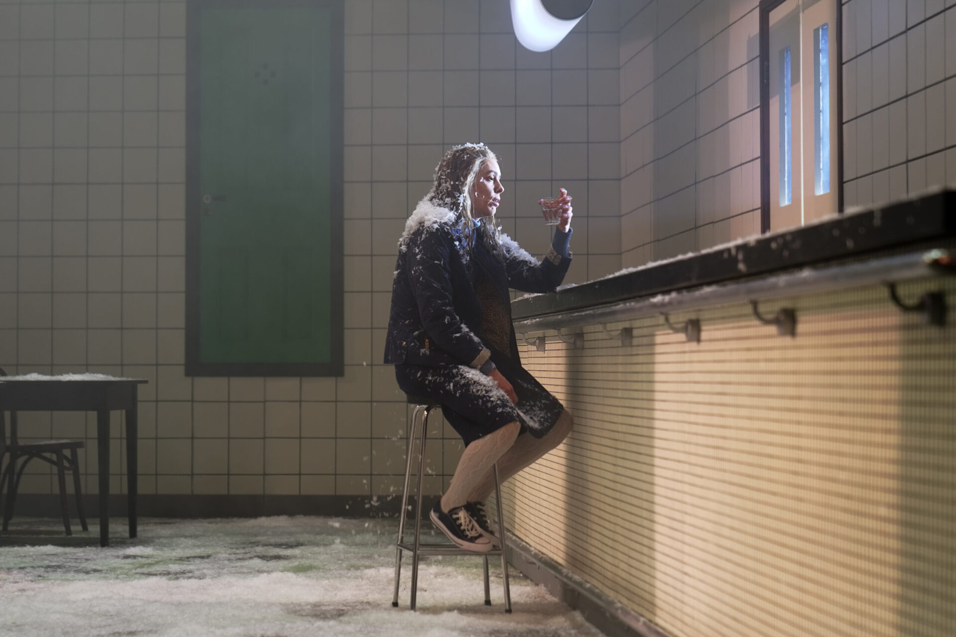 Kvinne sitter ved bardisk i et lokale fylt av snø