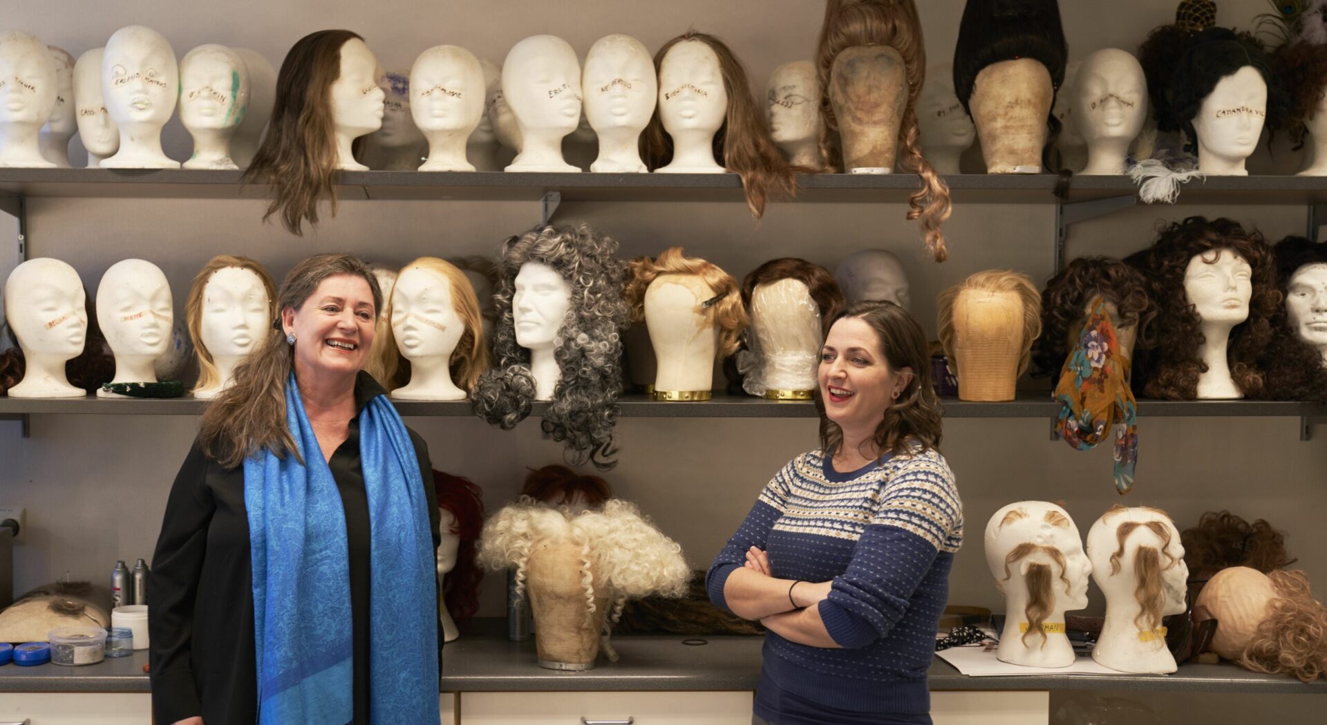Ansatte i sminkestuen står foran en vegg fylt med parykker.