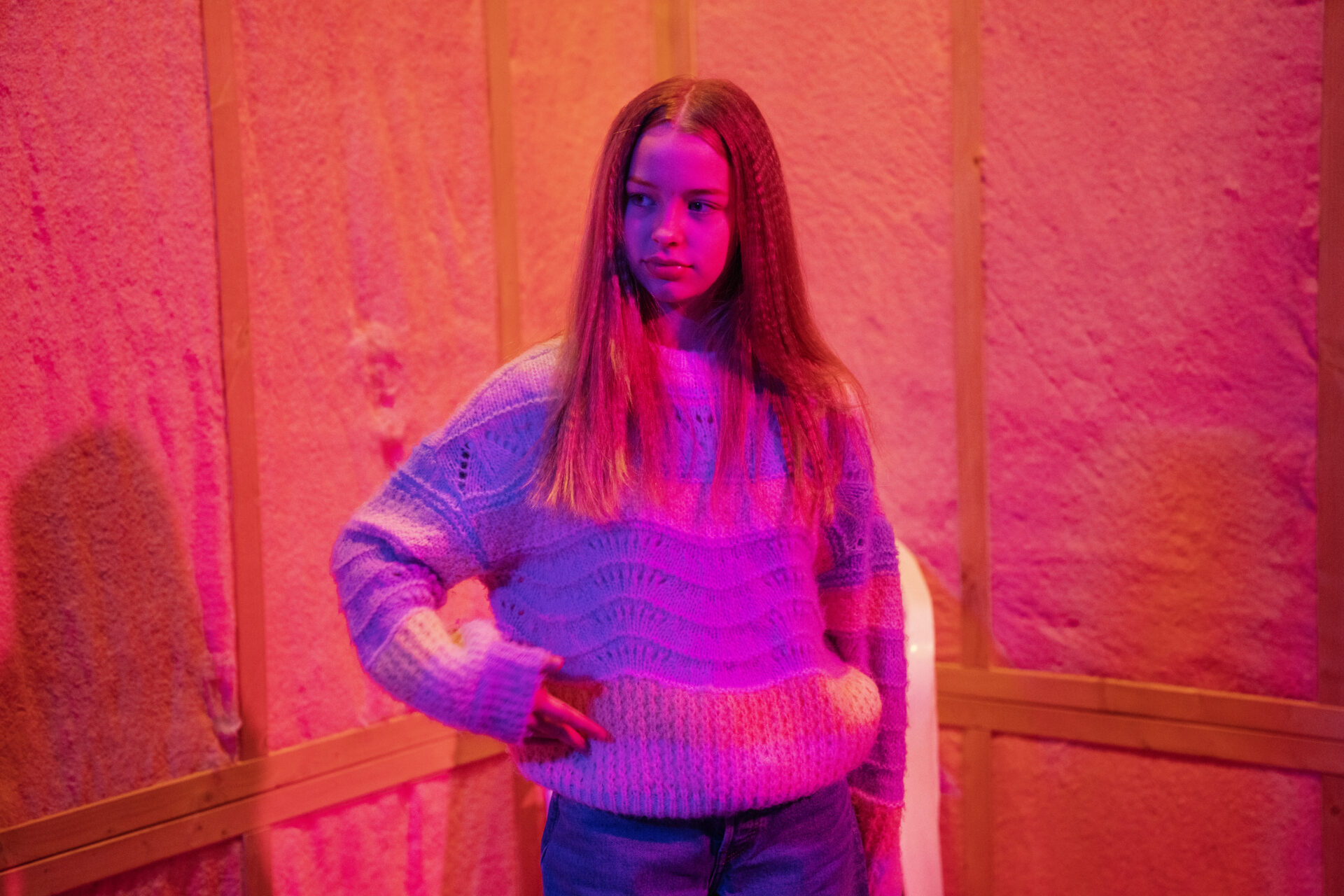 En ung kvinne med langt hår står og ser ut i rommet.