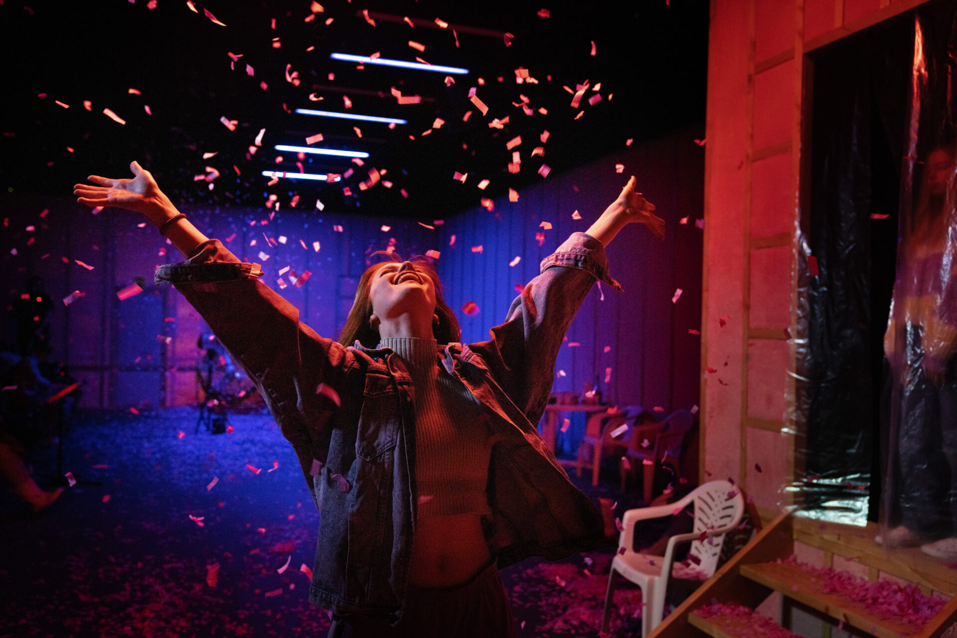 En ung kvinne strekker armene i været og smiler mens det regner konfetti over henne.