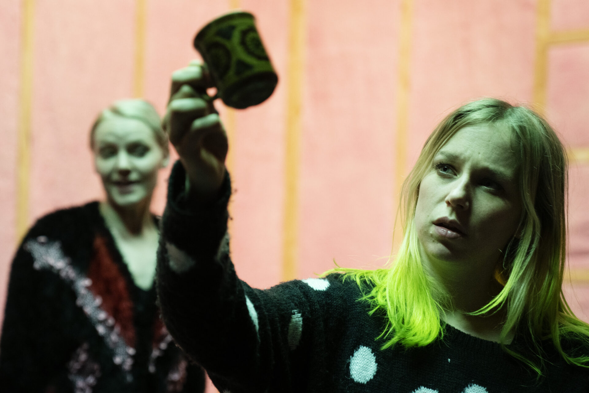 En kvinne løfter en kopp mens en annen står bak og ser på