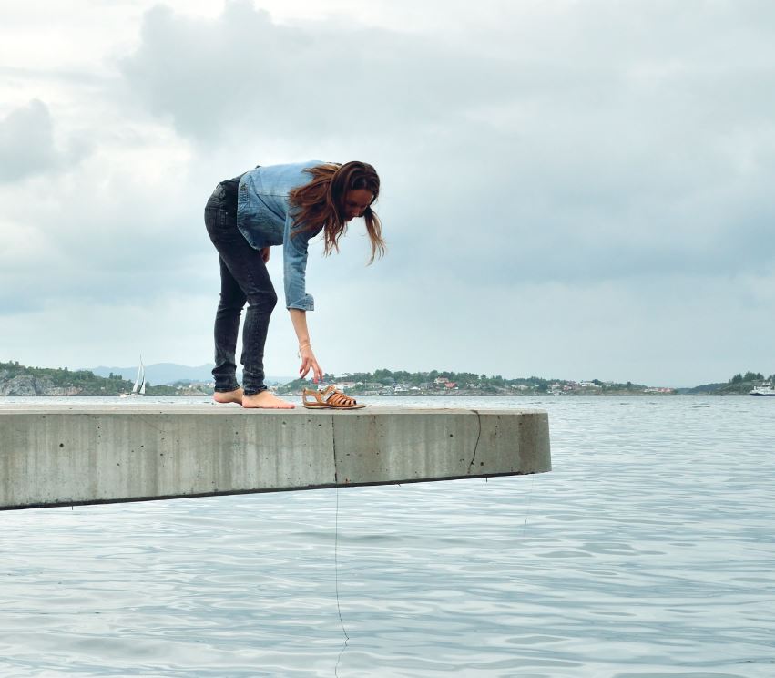 Ragnhild som står på kanten av en betongbrygge og griper tak i et par sko