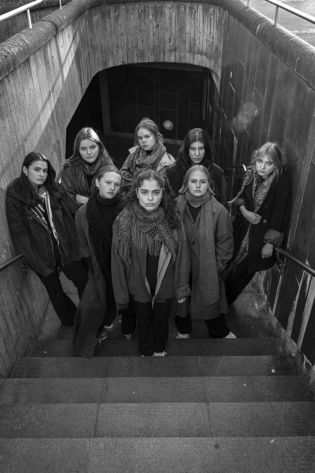 Åtte jenter som står i bunnen av en trappeoppgang og kikker opp