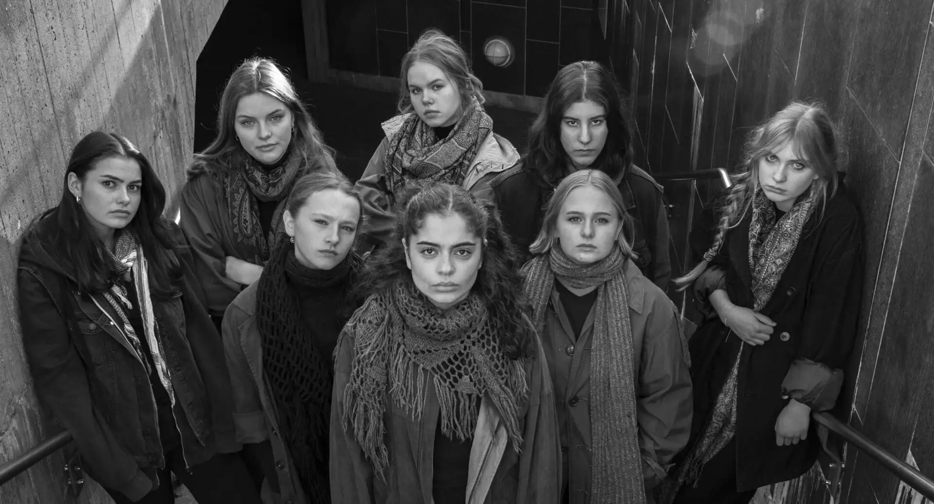 Åtte jenter som står i bunnen av en trappeoppgang og kikker opp