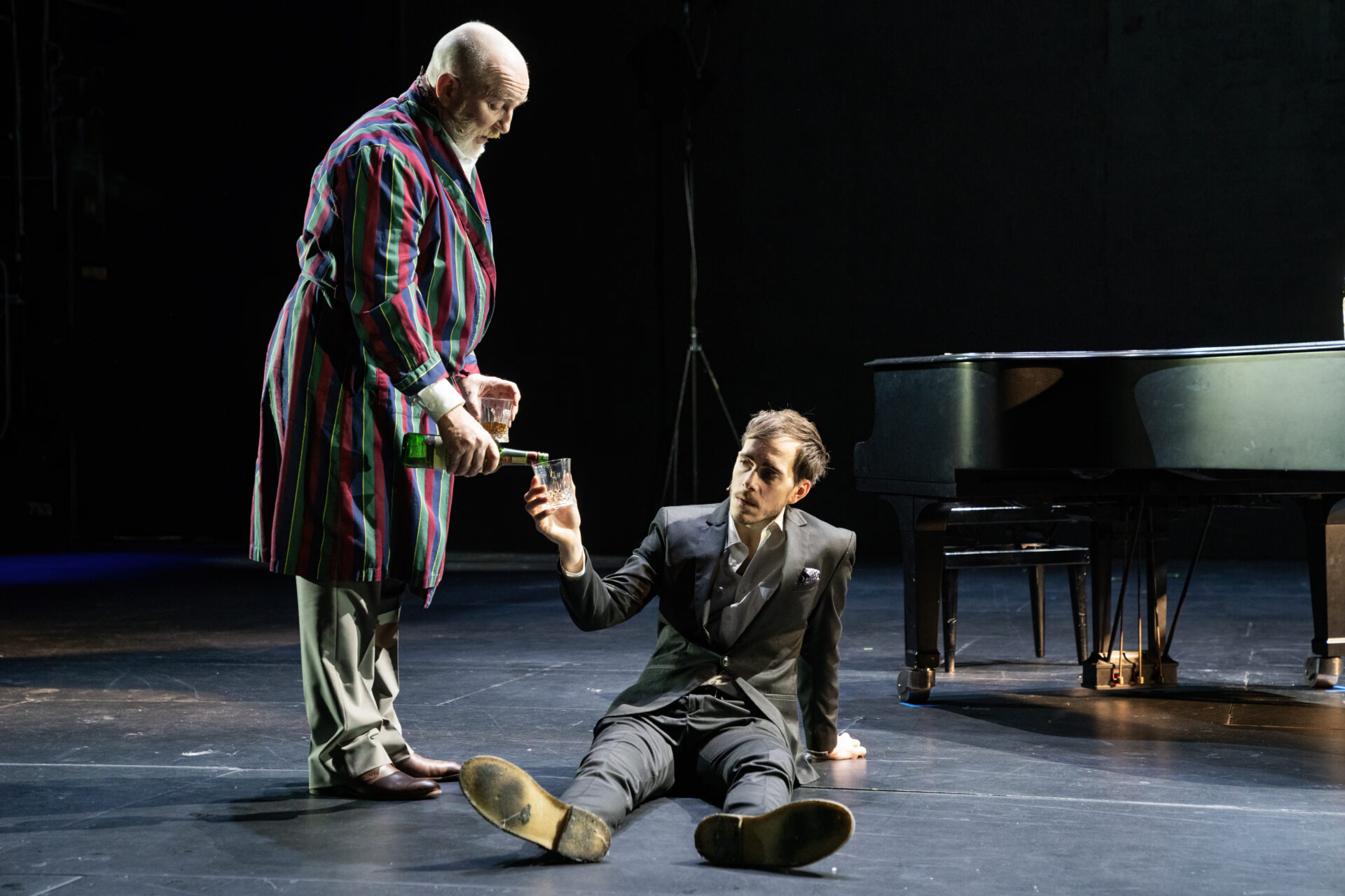 Full sønn som sitter på gulvet og får påfyll i glasset av sin far.