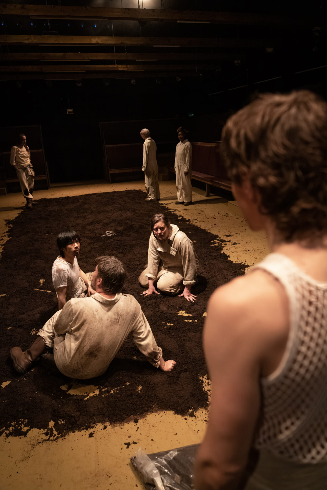 Menn og kvinner som sitter i gjørma og ser mot en mann som taler