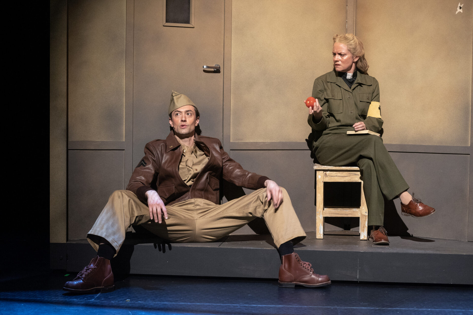 En feltprest med en tomat i hånden og en soldat som sitter inntil en vegg