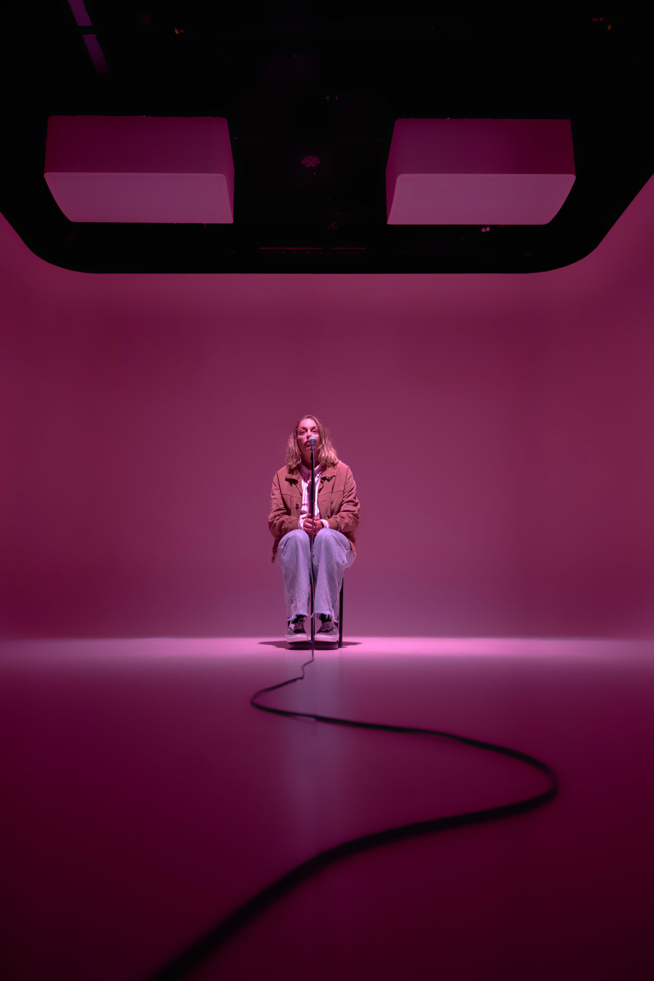 Kvinne som sitter på en krakk og snakker i en mikrofon, i et rosa rom