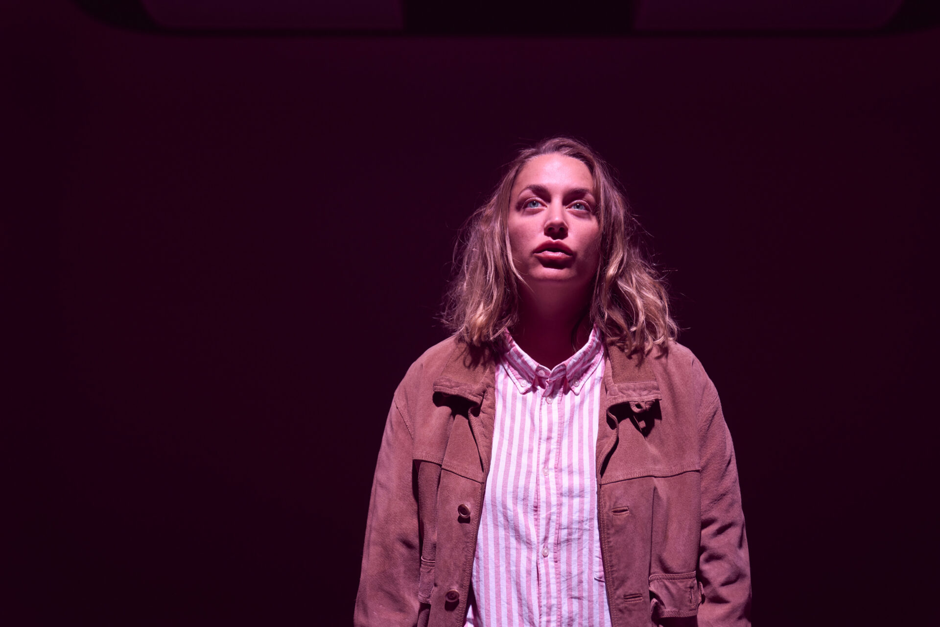 En kvinne i stripete skjorte, som står i et tomt rom og titter opp