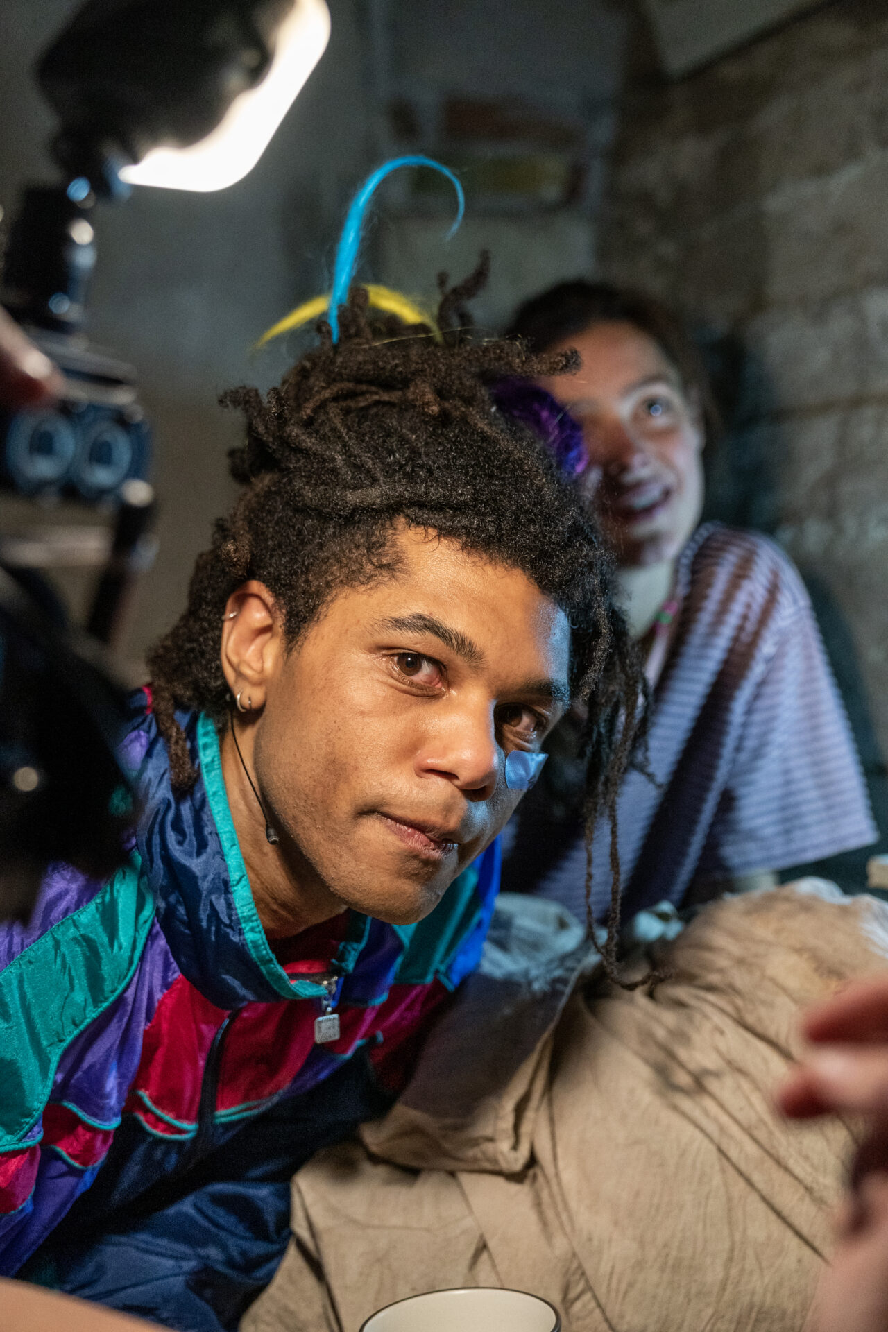 En mannlig skuespiller som titter rett i kamera, med en kvinne i bakgrunnen