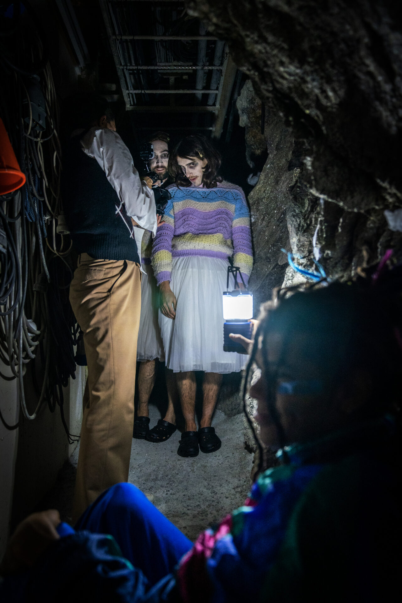 To menn med parykk kledd ut som jenter, i en mørk grotte