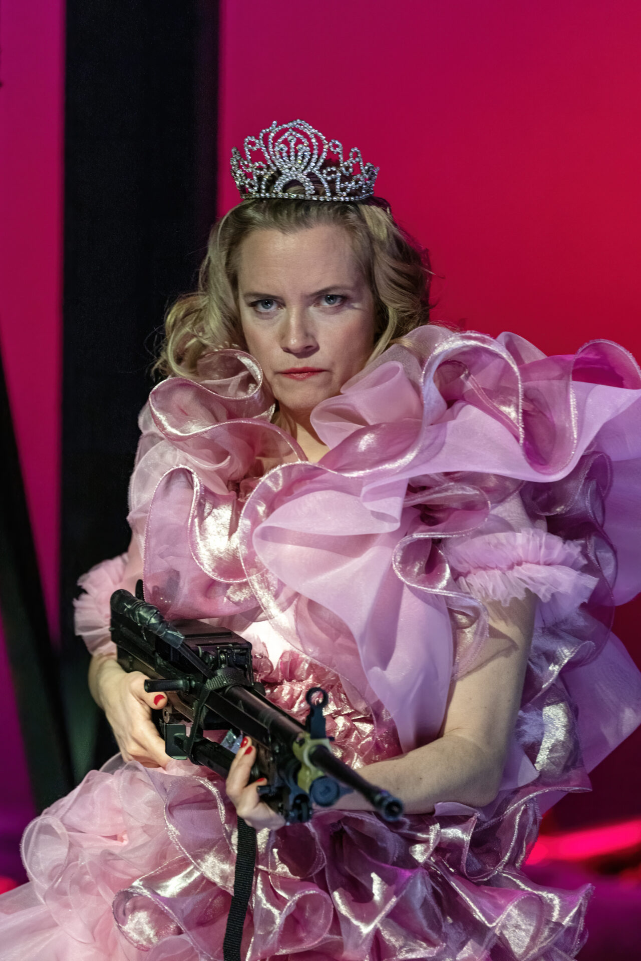 EN kvinne i en rosa kjole og tiara med maskingevær i hendene