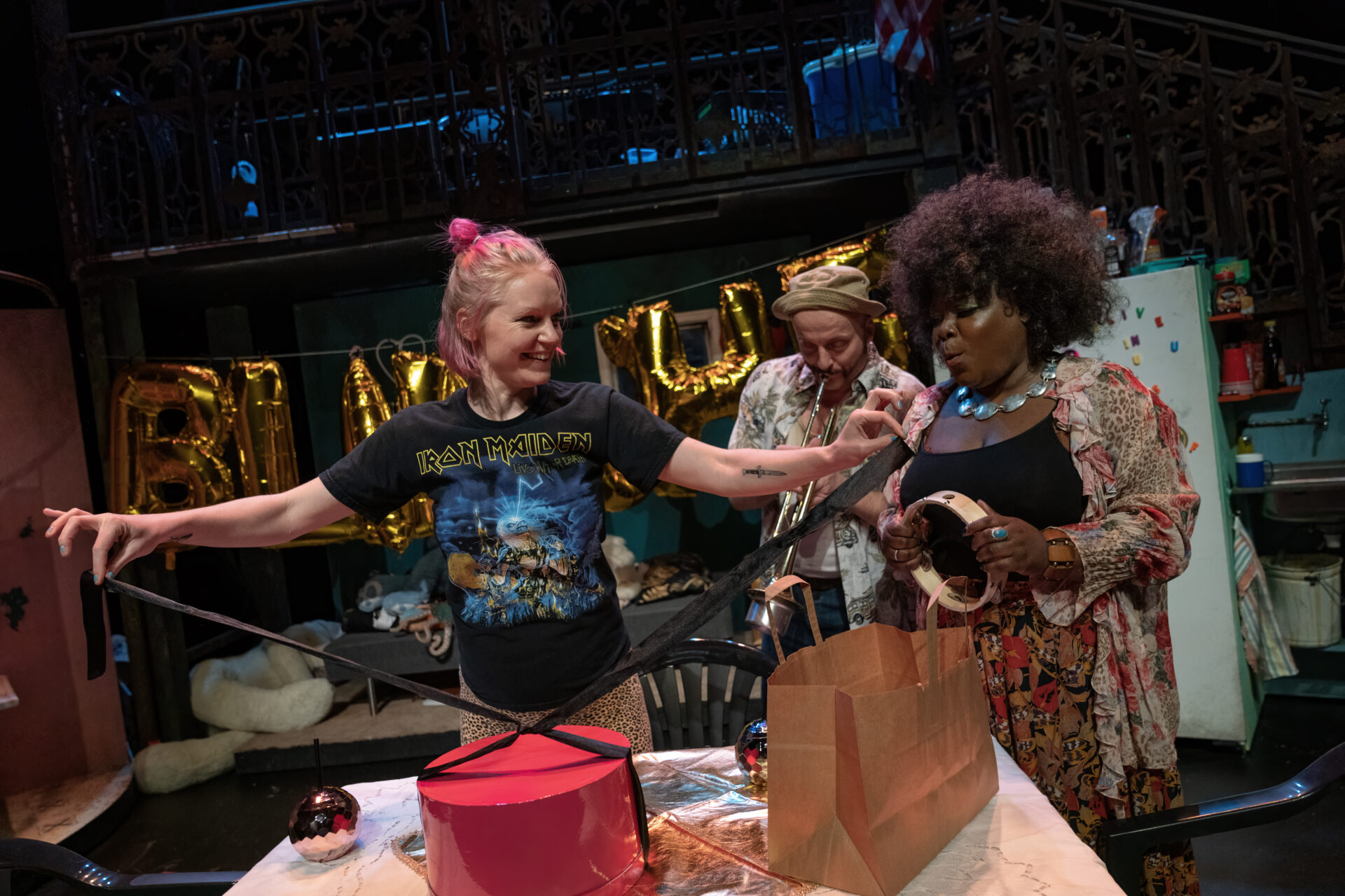 To kvinner er i gang med å pakke inn en gave. I bakkgrunnen spiller en mann trompet.