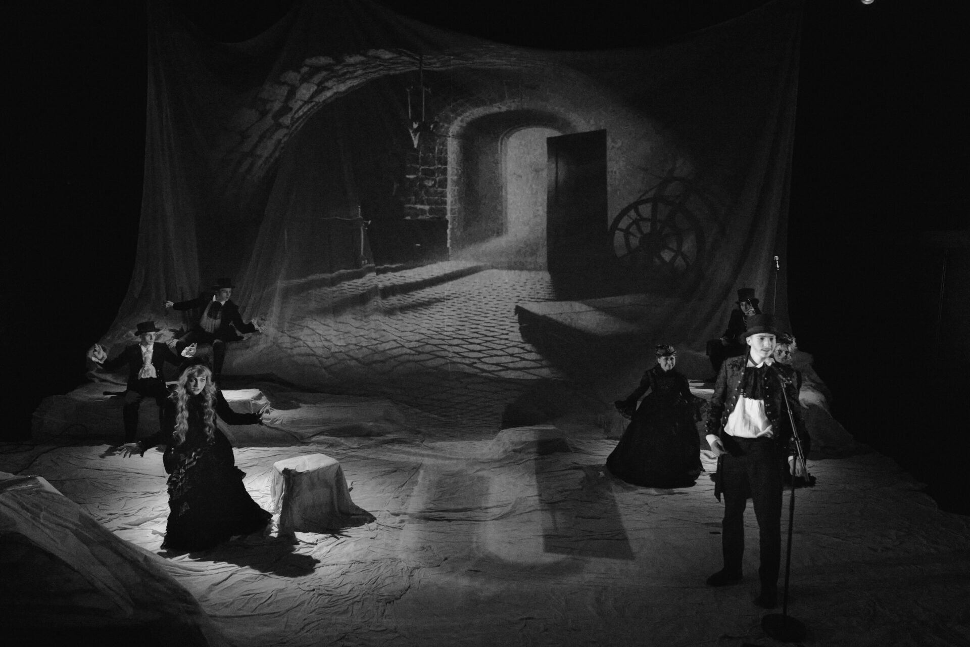 Nede i kjeller med døren vidåpen sees en mann som snakker i en mikrofon. Bak sitter to menn og to kvinner.