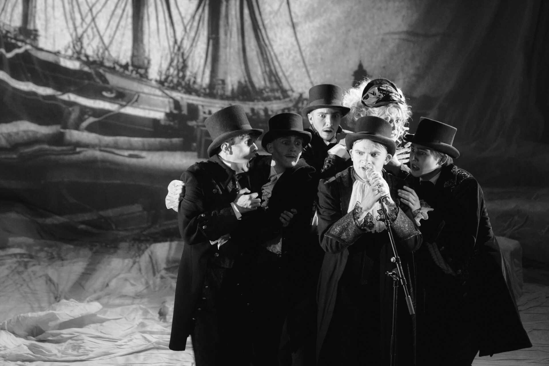 En mann snakker i mikrofon omkranset av en gruppe mennesker som er redde.