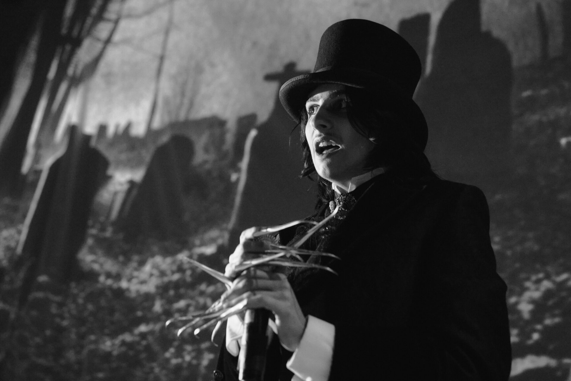 Hann med flosshatt som står foran et lerret med en kirkegård på