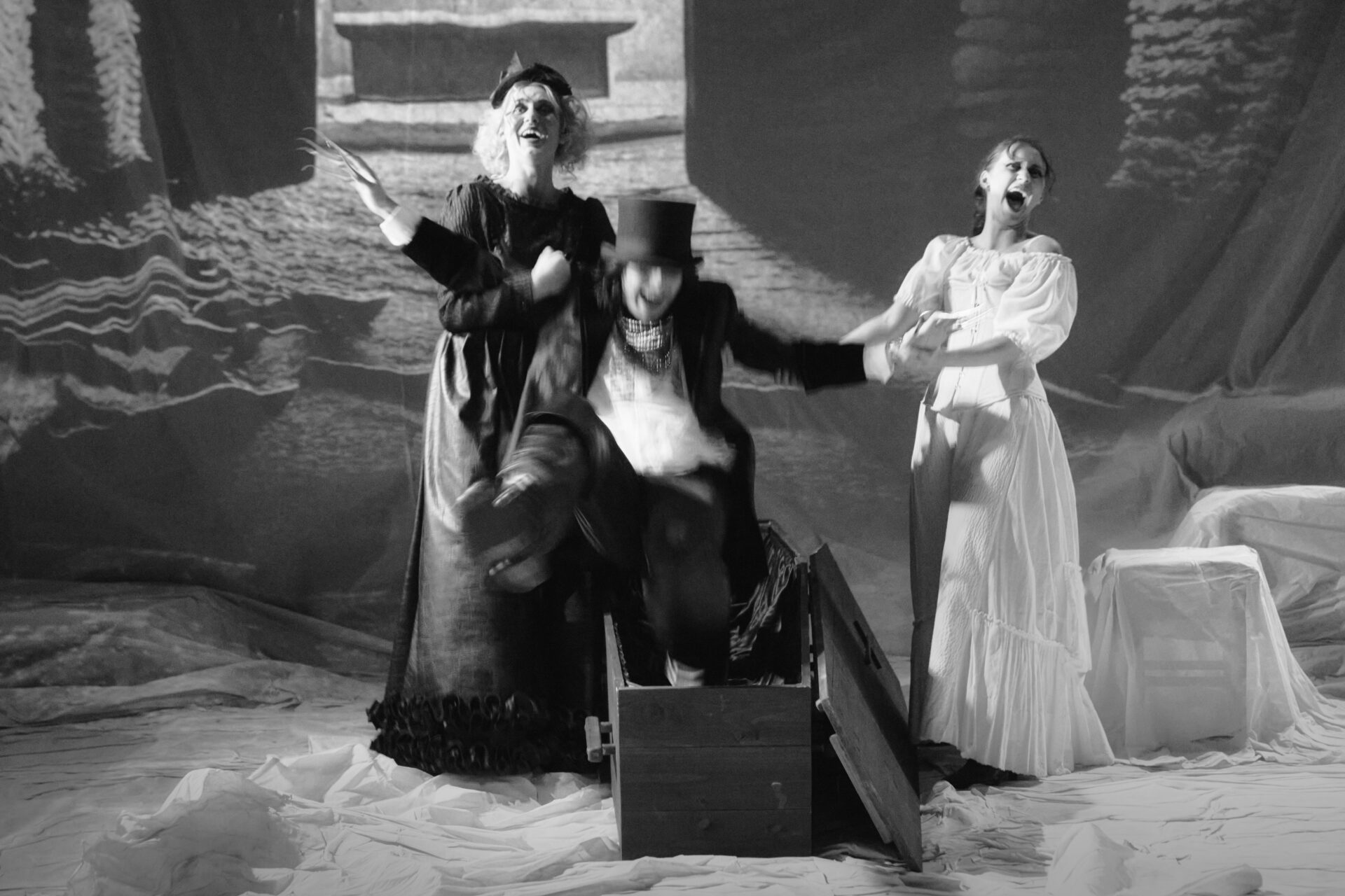 To kvinner ler når en mann kommer hoppende opp av en kiste