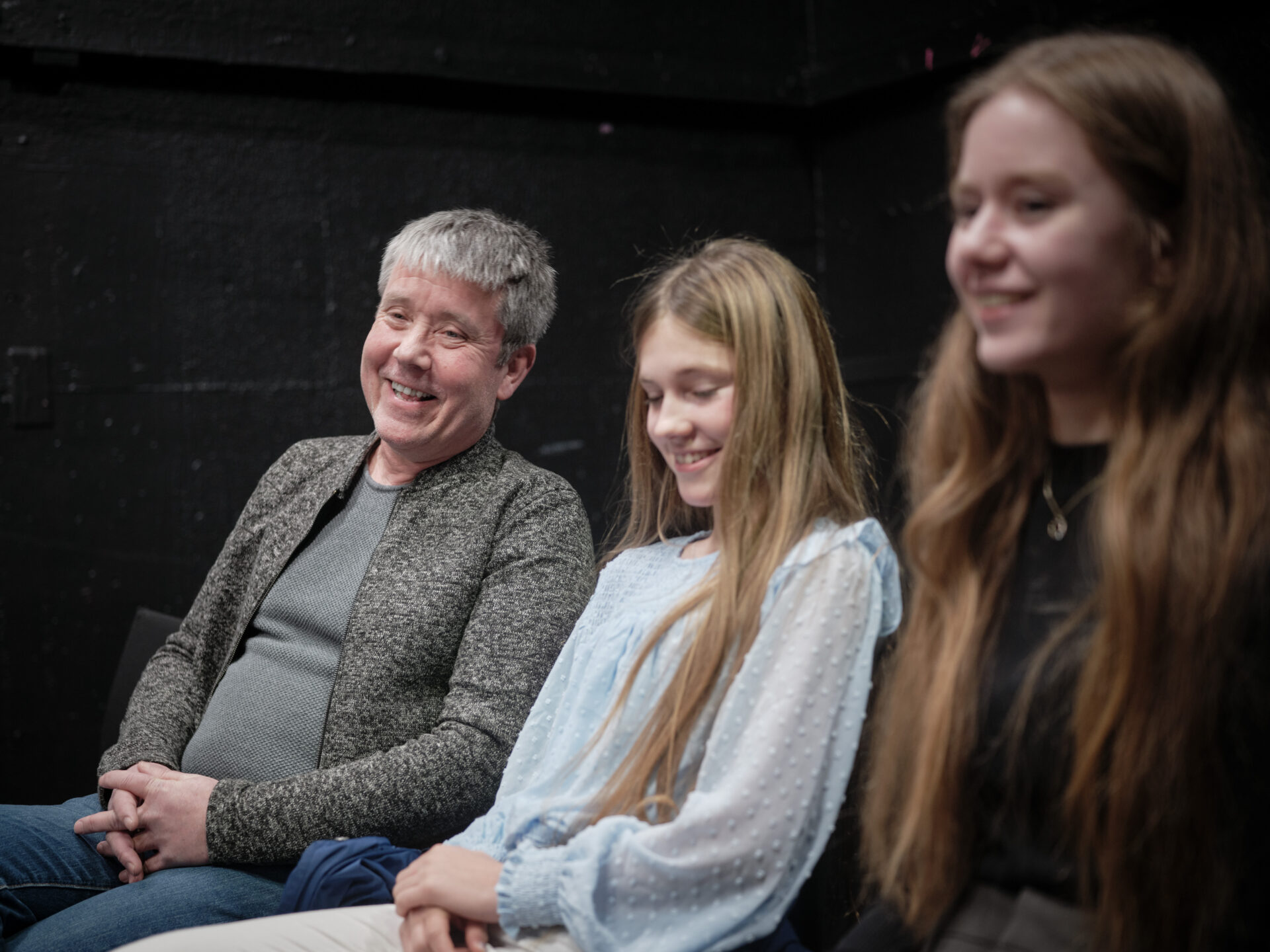 EN mann og hans to døtre sitter og smiler mot fotografen