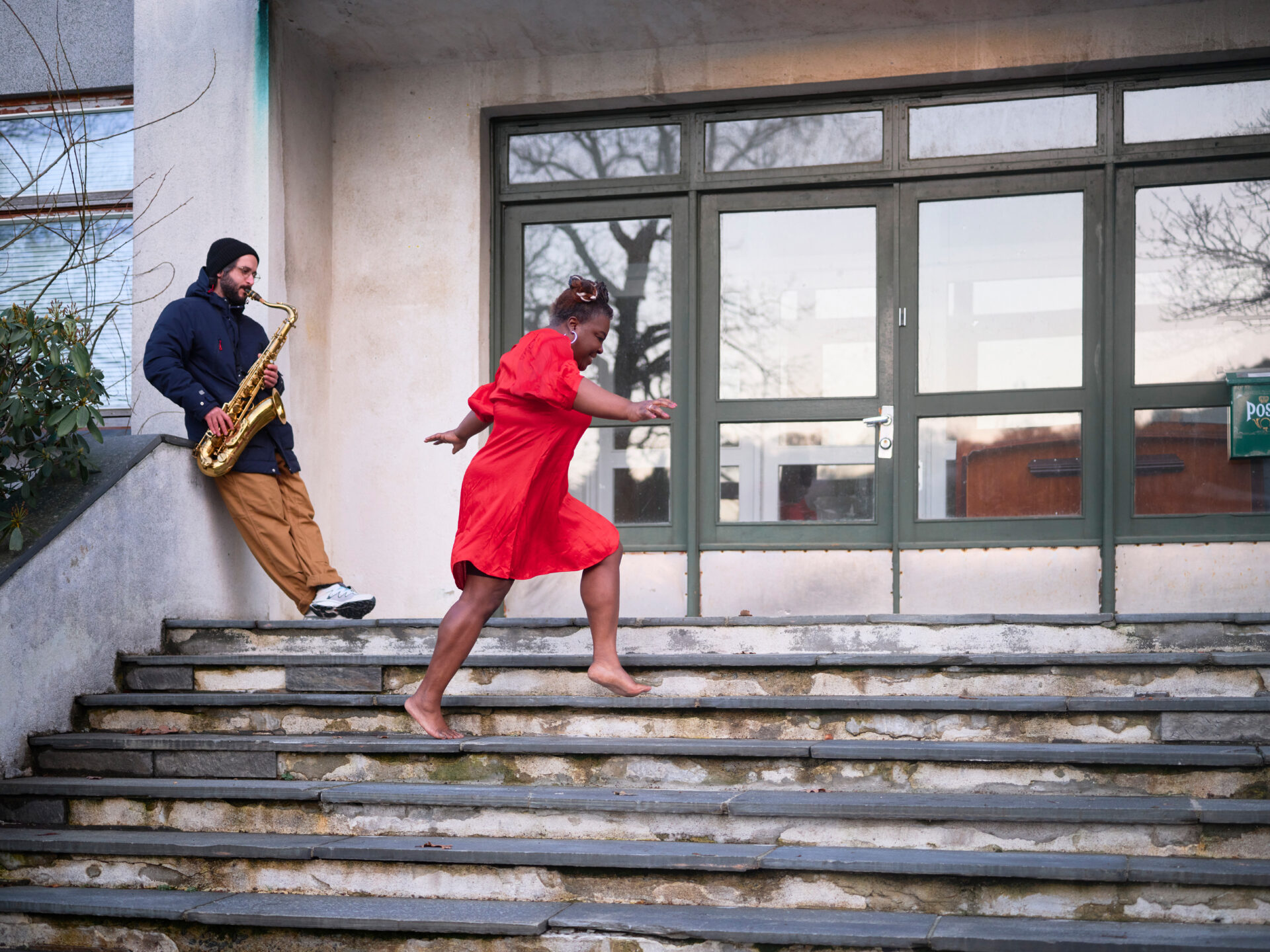 EN kvinne i rød kjole løper opp trappene og forbi en saxofonspillende mann
