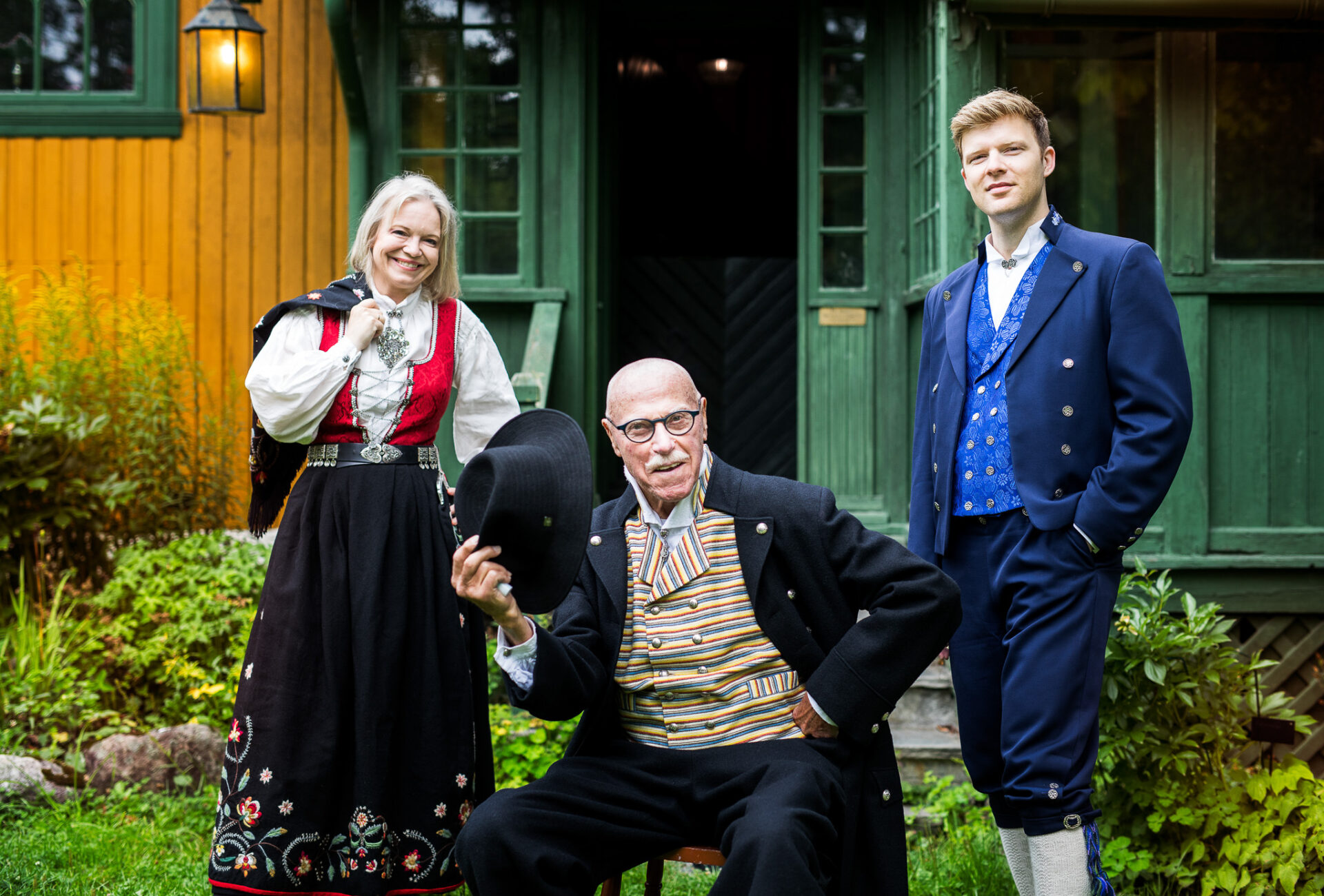 bilde av en kvinne og to menn foran et grønnmalt hus.