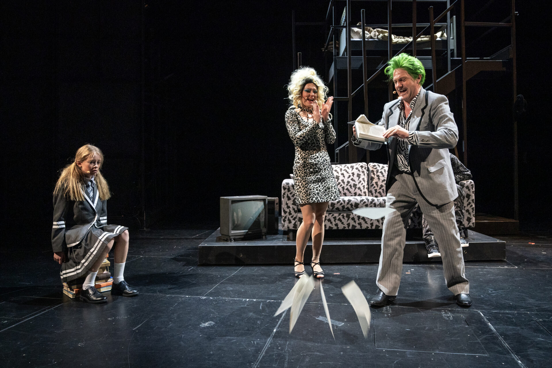 En mann river sider ut av en bok, mens en kvinne ler og klapper i hendene. Ved siden av sitter er trist pike og ser på.