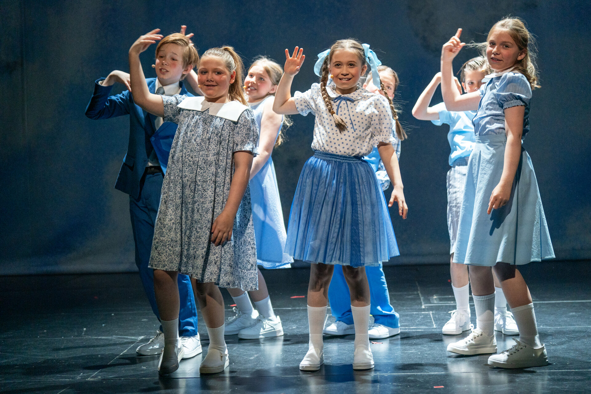 Syv barn i blåe klær smiler ut til publikum