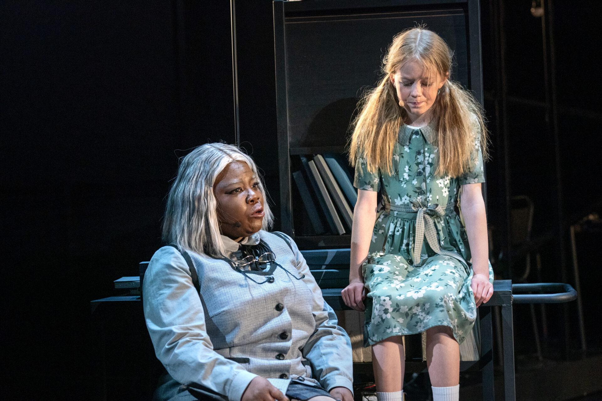 En jente sitter på en bibliotekstralle og snakker med en snill dame