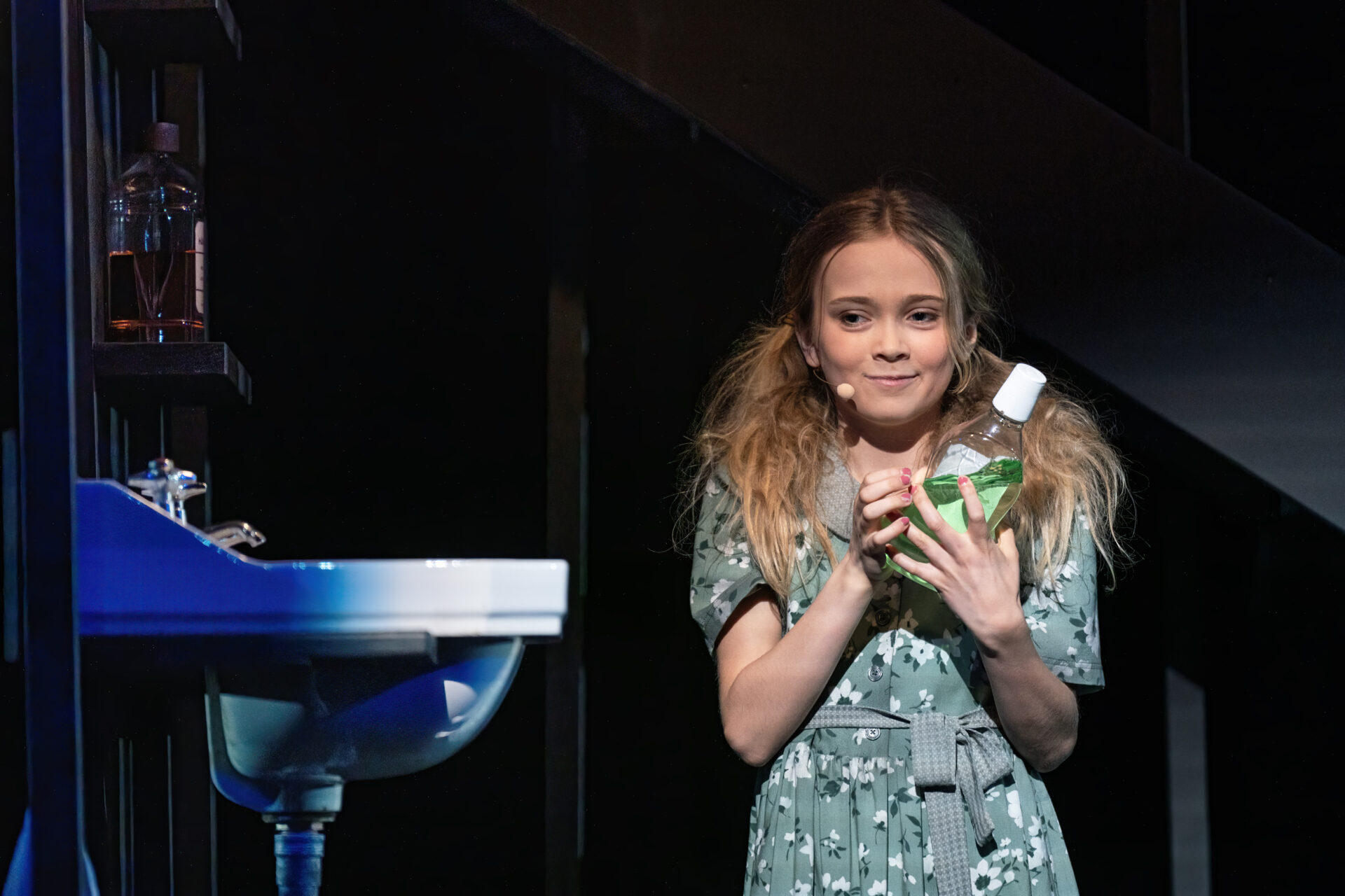 En liten jente står med en flaske grønn hårfarge i hånden