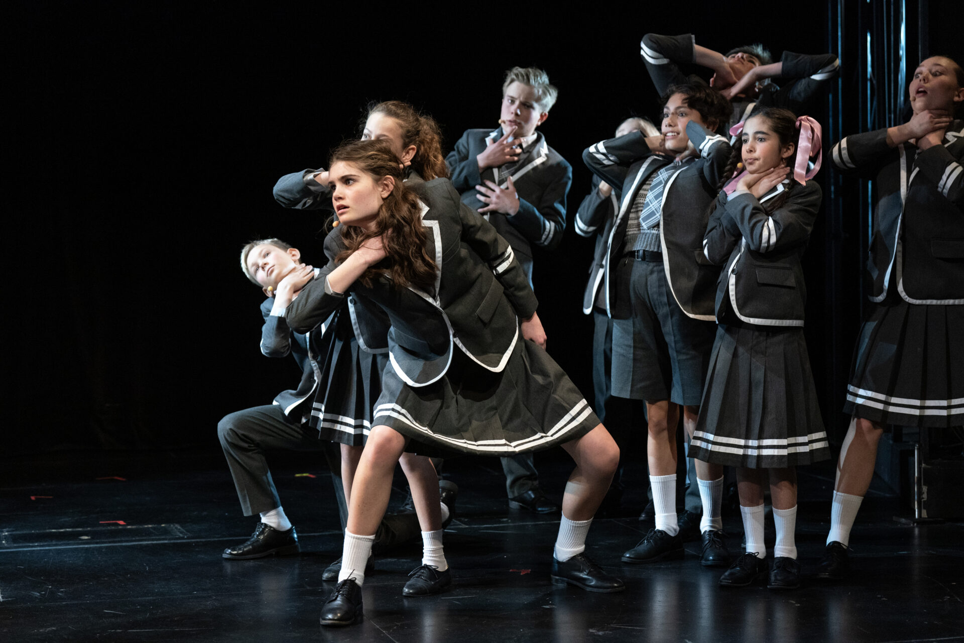 Flere barn danser og holder seg til halsen som om de kveles - fra stykket Matilda