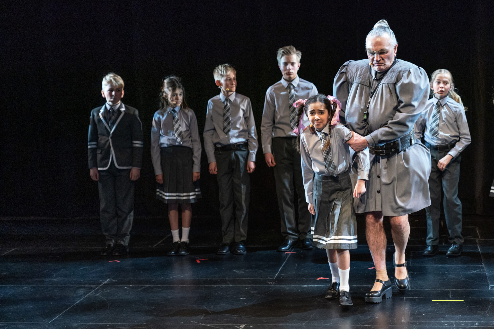 En rektor tar tak i armen til en liten jente og trekker henne ut av rekken av barn - fra stykket Matilda