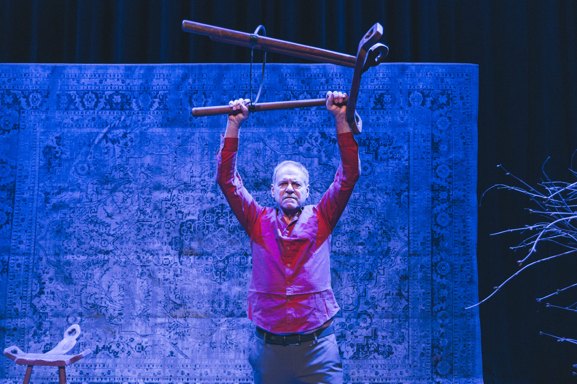 En mann i rød skjorte på scenen, som holder en krakk over hodet