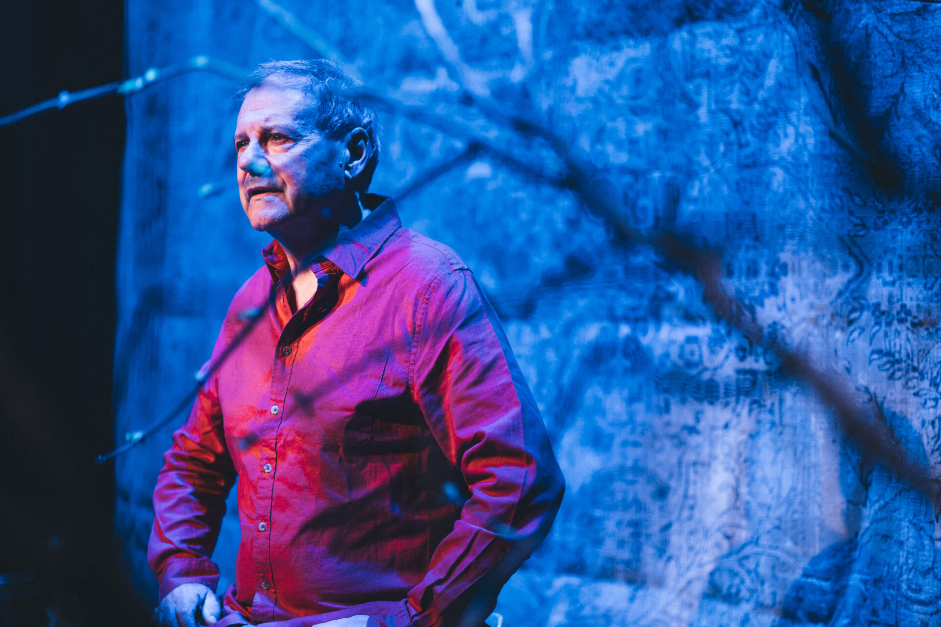 En mann i rød skjorte som sitter på en krakk på scenen, og titter utover