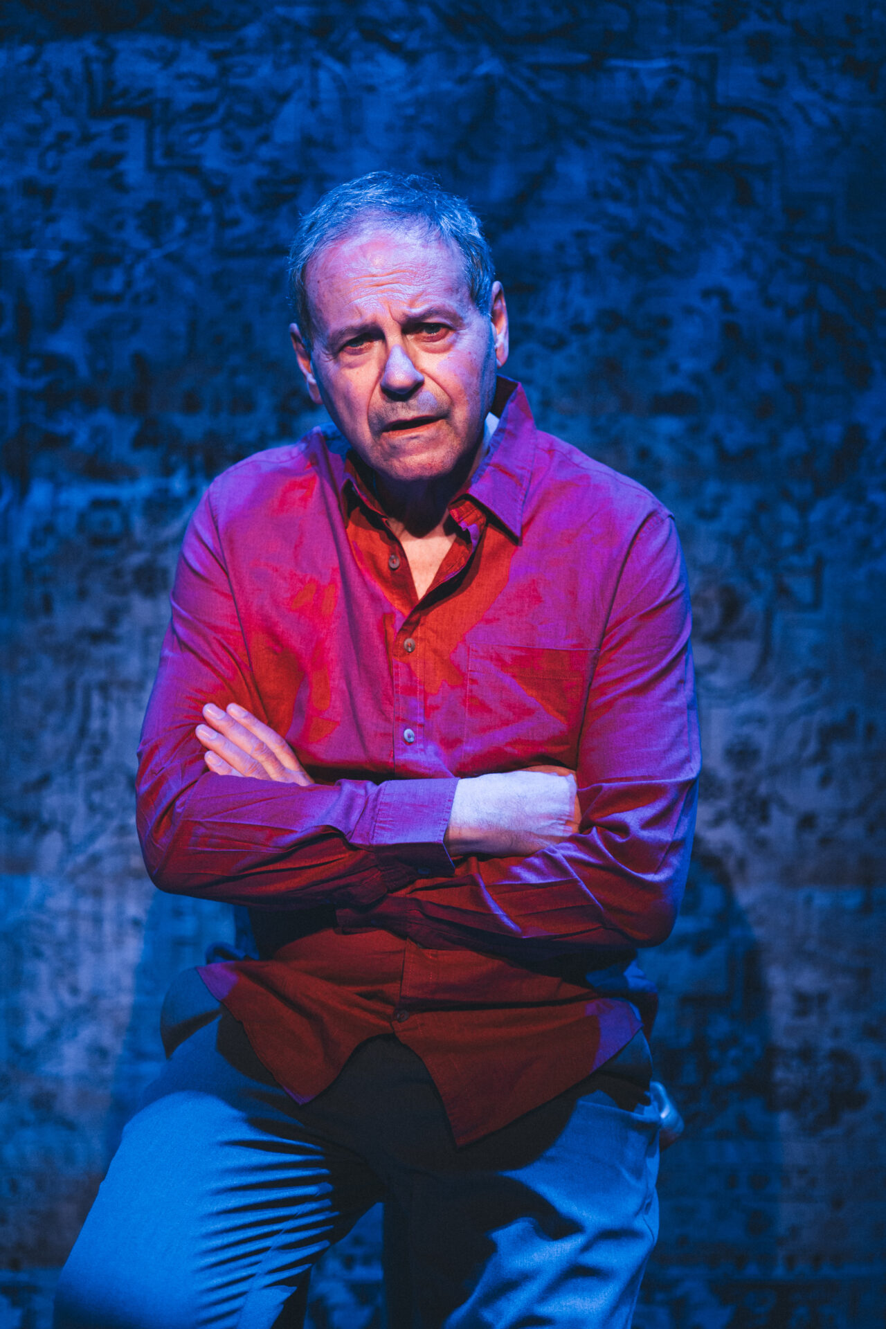 En mann som sitter på en krakk på scenen med armene i kors