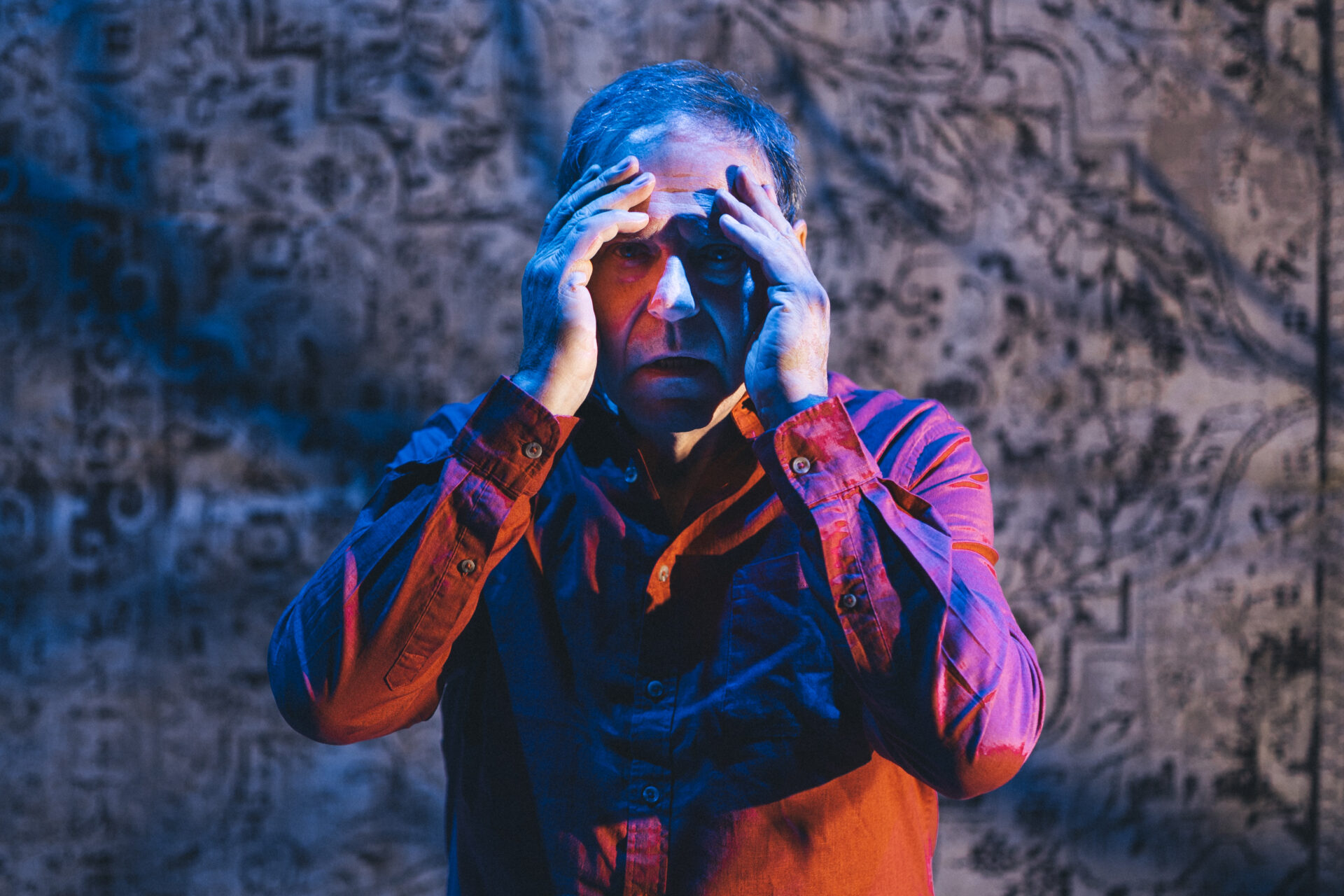 En mann som står på scenen og titter rett frem, med hendene opp til ansiktet