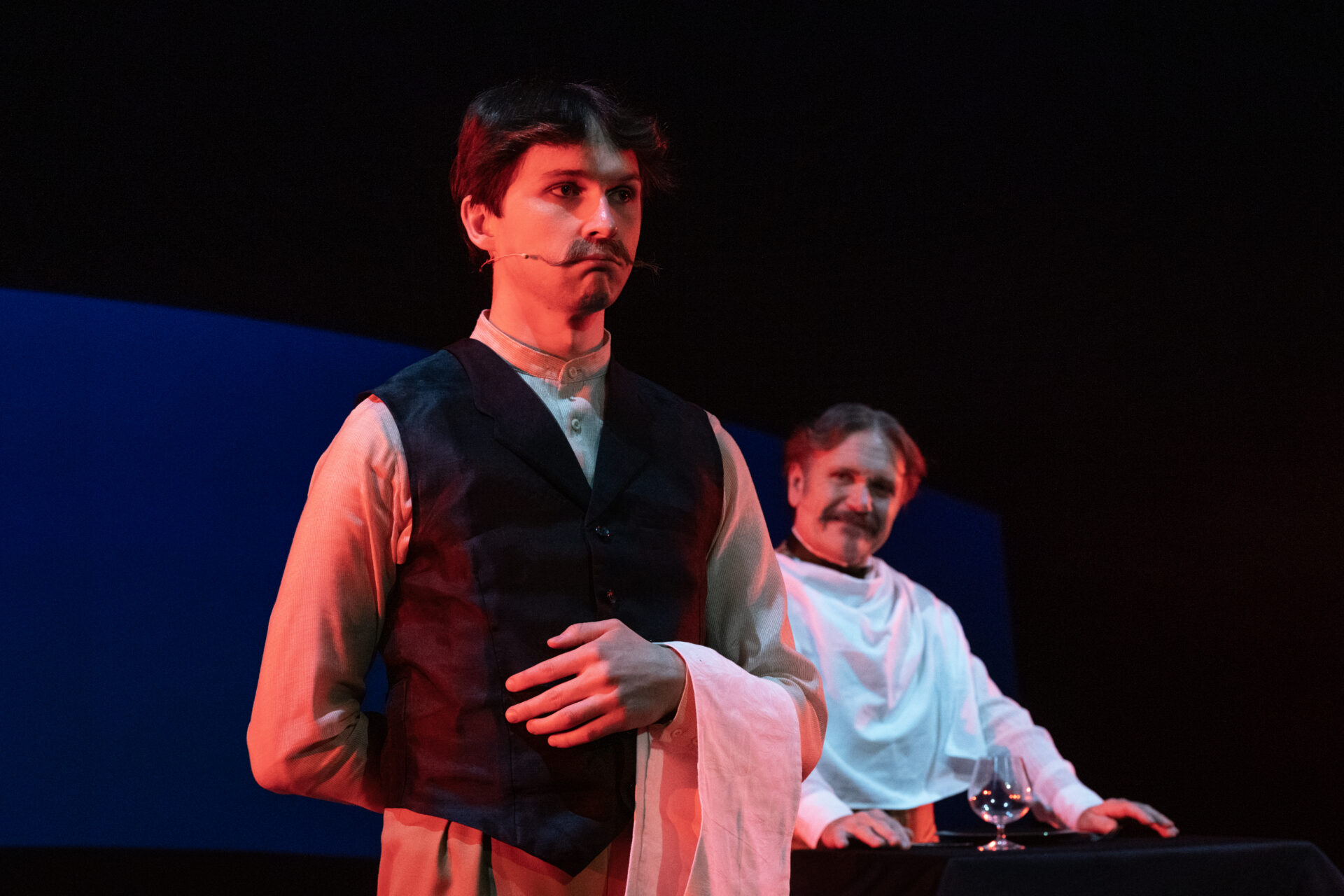 En mann med snurrebart som spiller hovmester