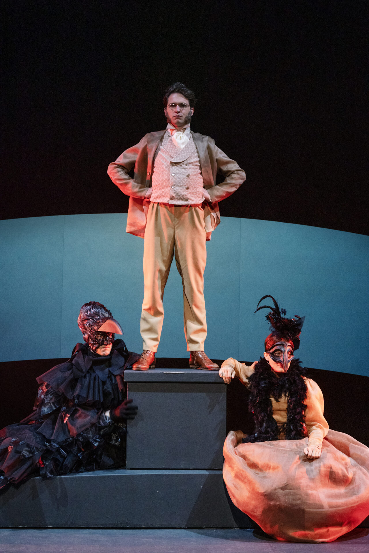 En mann som står på en pidestall, med to personer som spiller ravner på siden