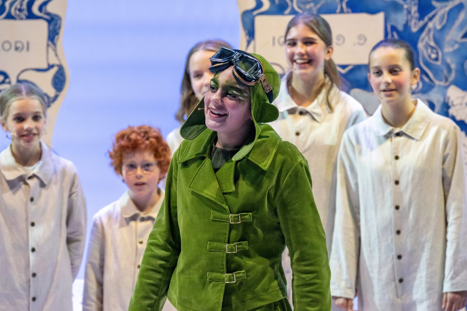 En gresshoppe synger med mange smilende barn i bakgrunnen